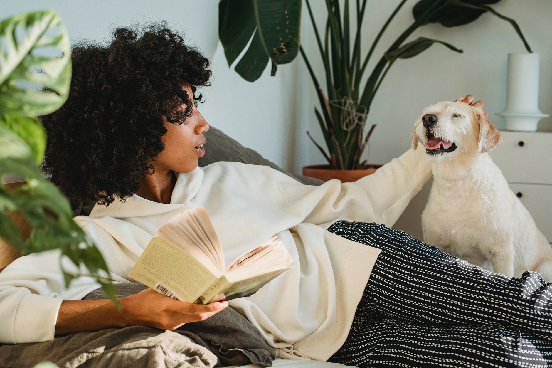 black woman caressing dog while relaxing with book